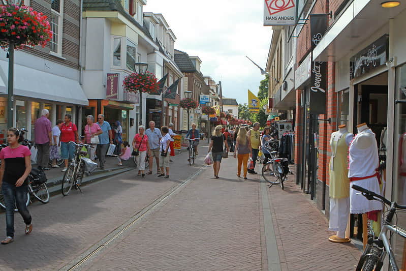 Gezellige winkelstraat in Driebergen met mensen, fietsen en hangende bloemenmanden, ideale omgeving voor een verblijf.